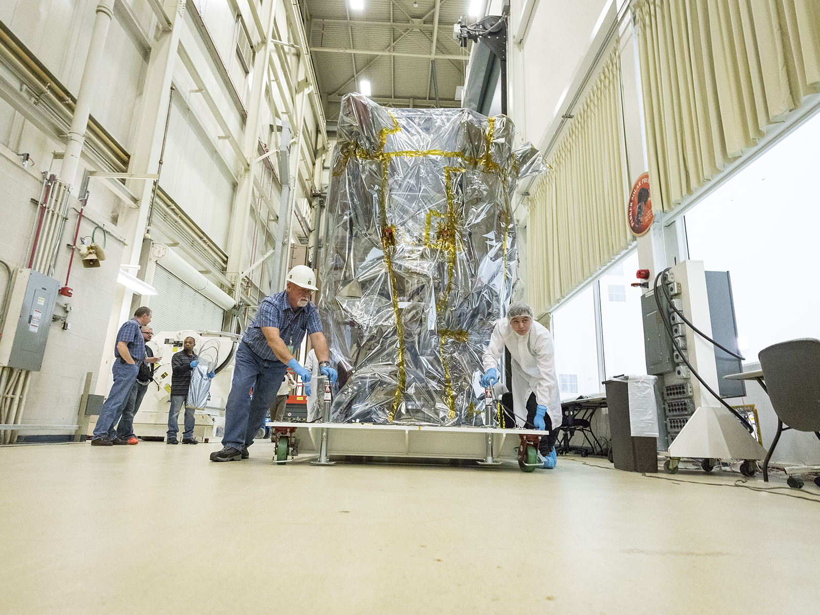 Member of the NASA Parker Solar Probe team wheel the spacecraft – bagged to protect it from contamination – from its cleanroom at NASA’s Goddard Space Flight Center in Greenbelt, Md., to the thermal vacuum chamber, where it will undergo approximately seven weeks of testing at extreme temperatures that will simulate the space environment. 