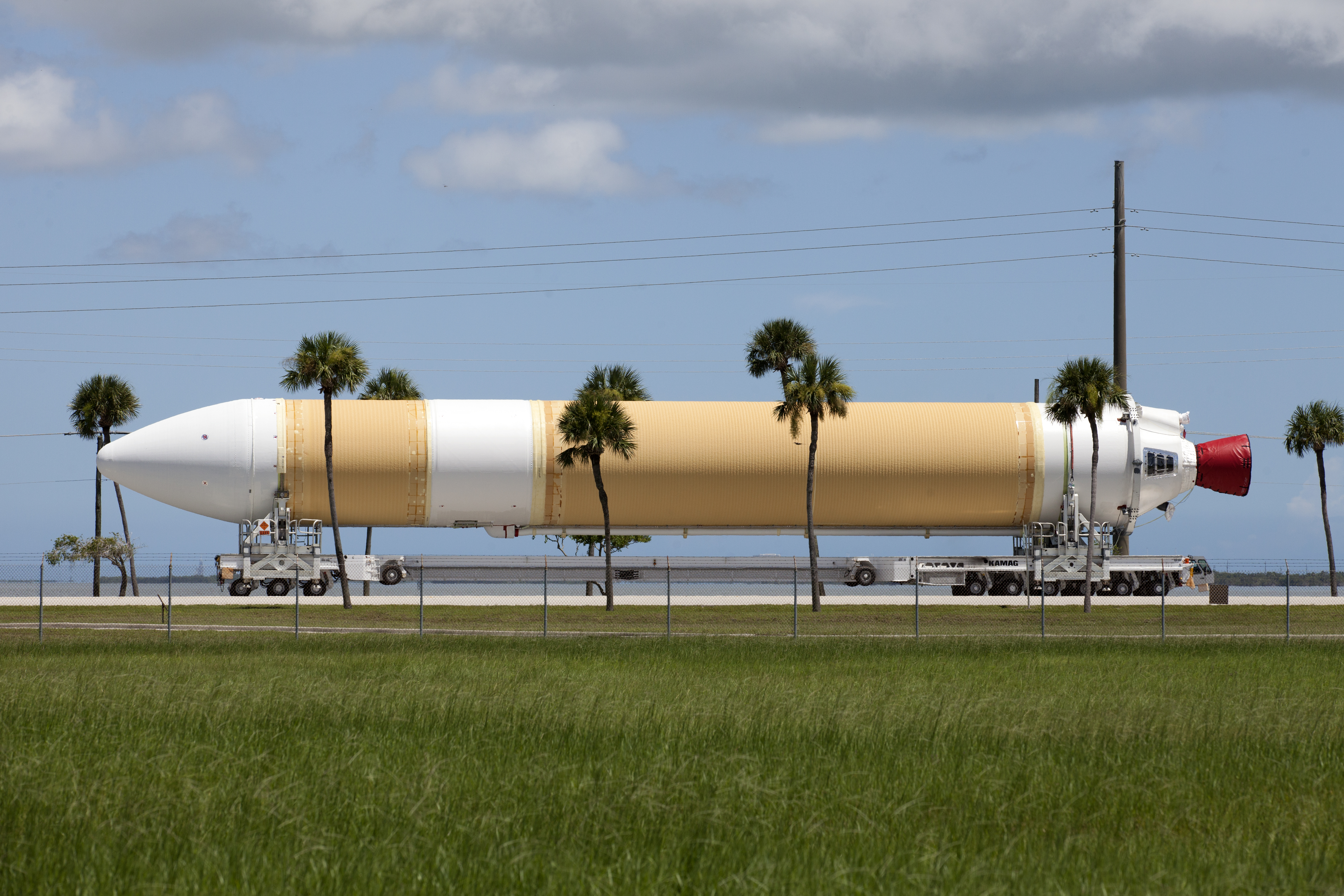 Framed by a series of cabbage palms, a United Launch Alliance Delta IV Heavy common booster core is transported by truck to Cape Canaveral Air Force Station’s Launch Complex 37 Horizontal Processing Facility after arriving at Port Canaveral. The Delta IV Heavy will launch NASA’s upcoming Parker Solar Probe mission. 