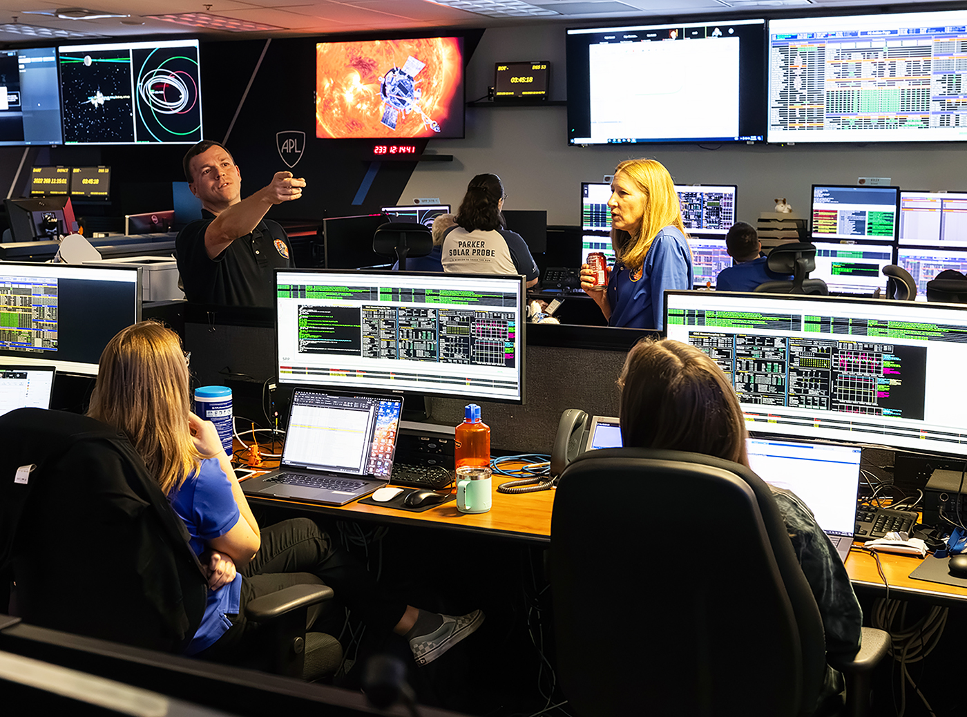 Standing, from left, Parker Solar Probe Mission Operations Manager Nick Pinkine and Project Manager Helene Winters discuss the progress of Parker's gravity assist flyby of Venus with members of the spacecraft operations team at the Johns Hopkins Applied Physics Laboratory on Aug. 21.